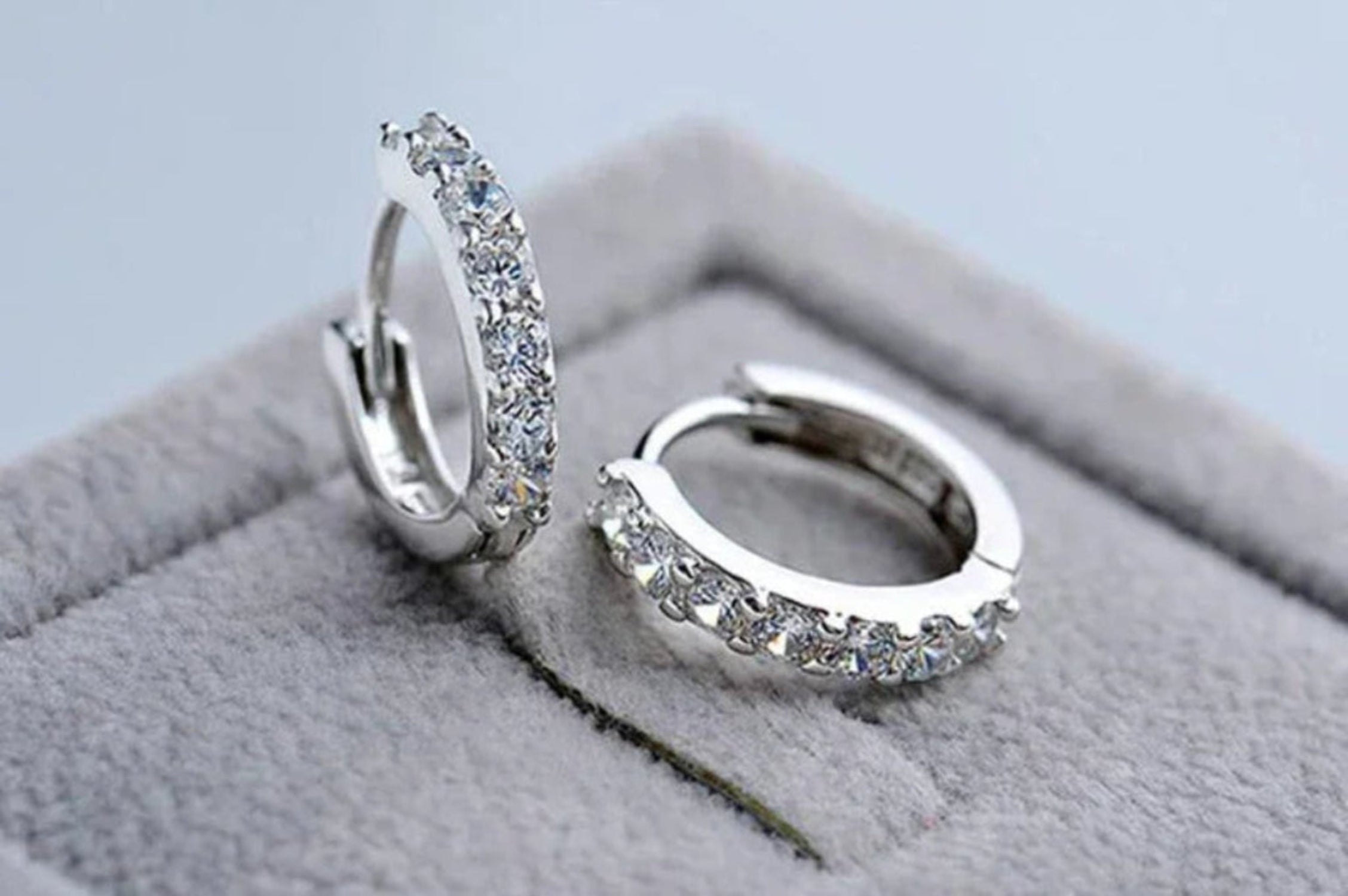 Pair of silver hoop earrings with clear stones on a soft gray surface